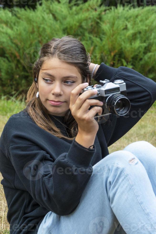 Portrait of a beautiful teenage girl having fun with a camera. A girl takes pictures outdoors with an old camera. photo