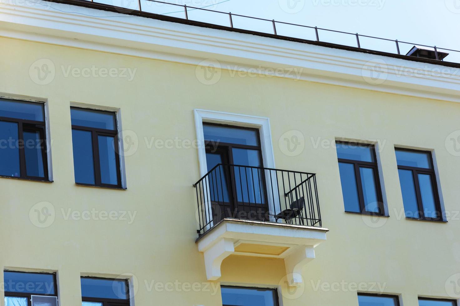 A small cute balcony with a chair on the facade of a yellow residential building, summer photo