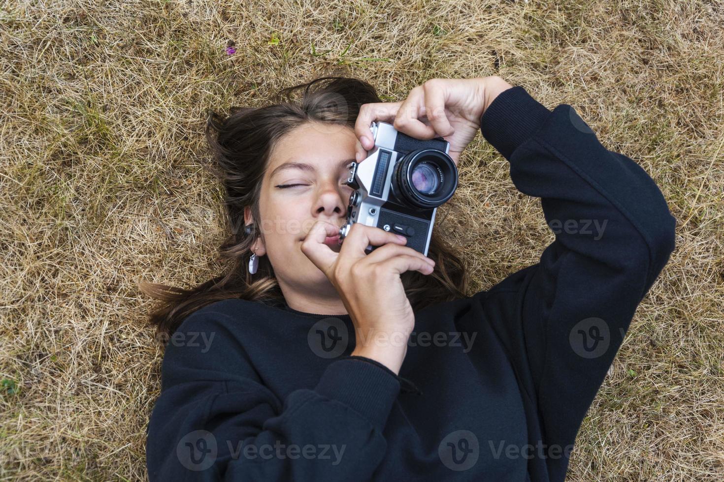 Cute teen girl with a camera, a girl taking pictures on a retro vintage camera on the grass in the park, a hobby concept photo