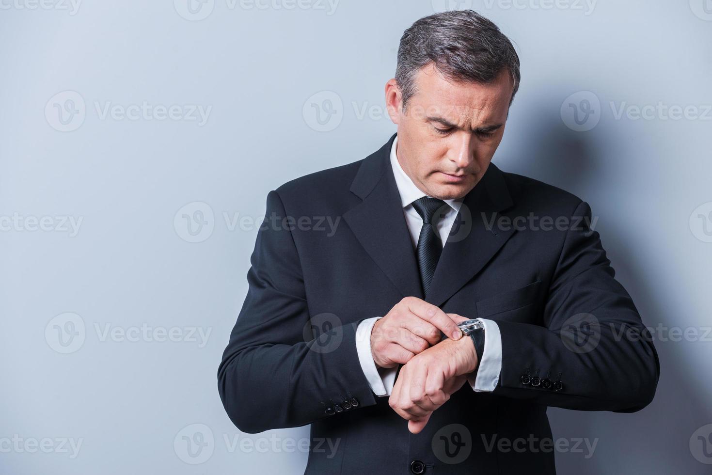Businessman checking the time. Confident mature man in formalwear checking the time while looking at his watch and standing against grey background photo