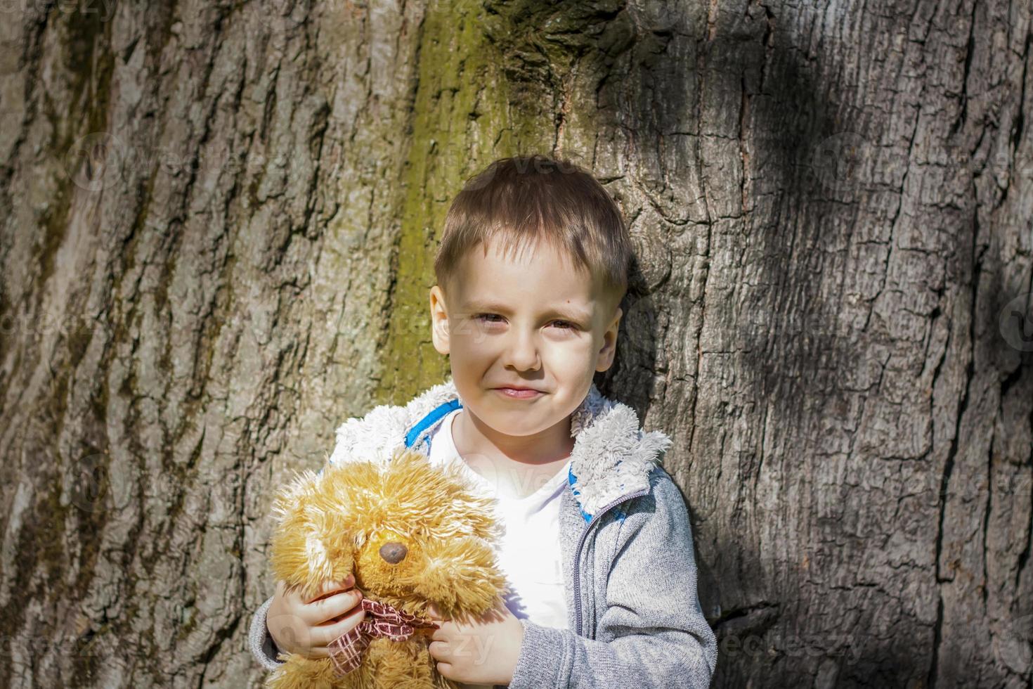 A cute boy is playing with a bear cub in the forest. The sun's rays envelop the space. A magical story of interactions for the book. Space for copying. photo