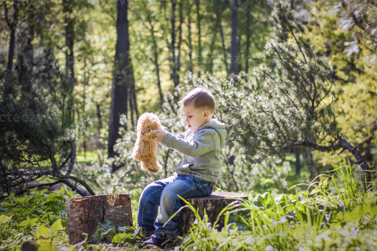 A cute boy is playing with a bear cub in the forest. The sun's rays envelop the space of the clearing with a stump. A magical story of interactions for the book. Space for copying. Selective photo