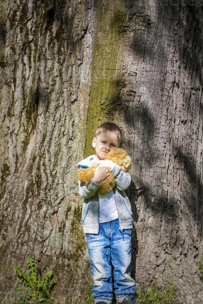 un chico lindo está jugando con un cachorro de oso en el bosque. los rayos del sol envuelven el espacio. una historia mágica de interacciones para el libro. espacio para copiar. foto