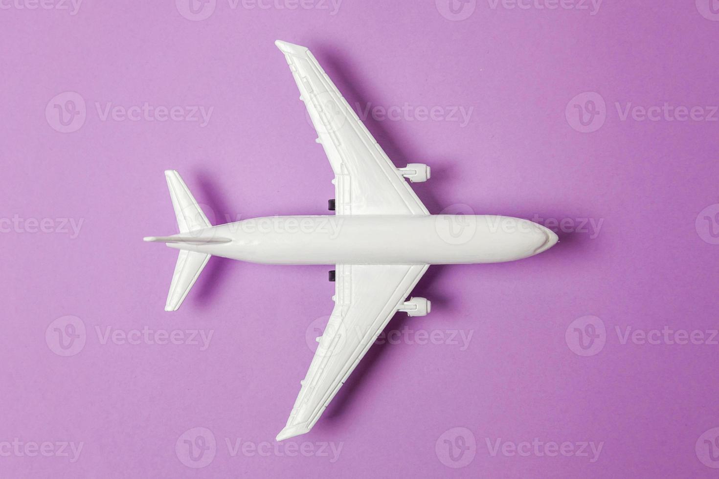 Simply flat lay design miniature toy model plane on violet purple pastel colorful paper trendy background. Travel by plane vacation summer weekend sea adventure trip journey ticket tour concept. photo