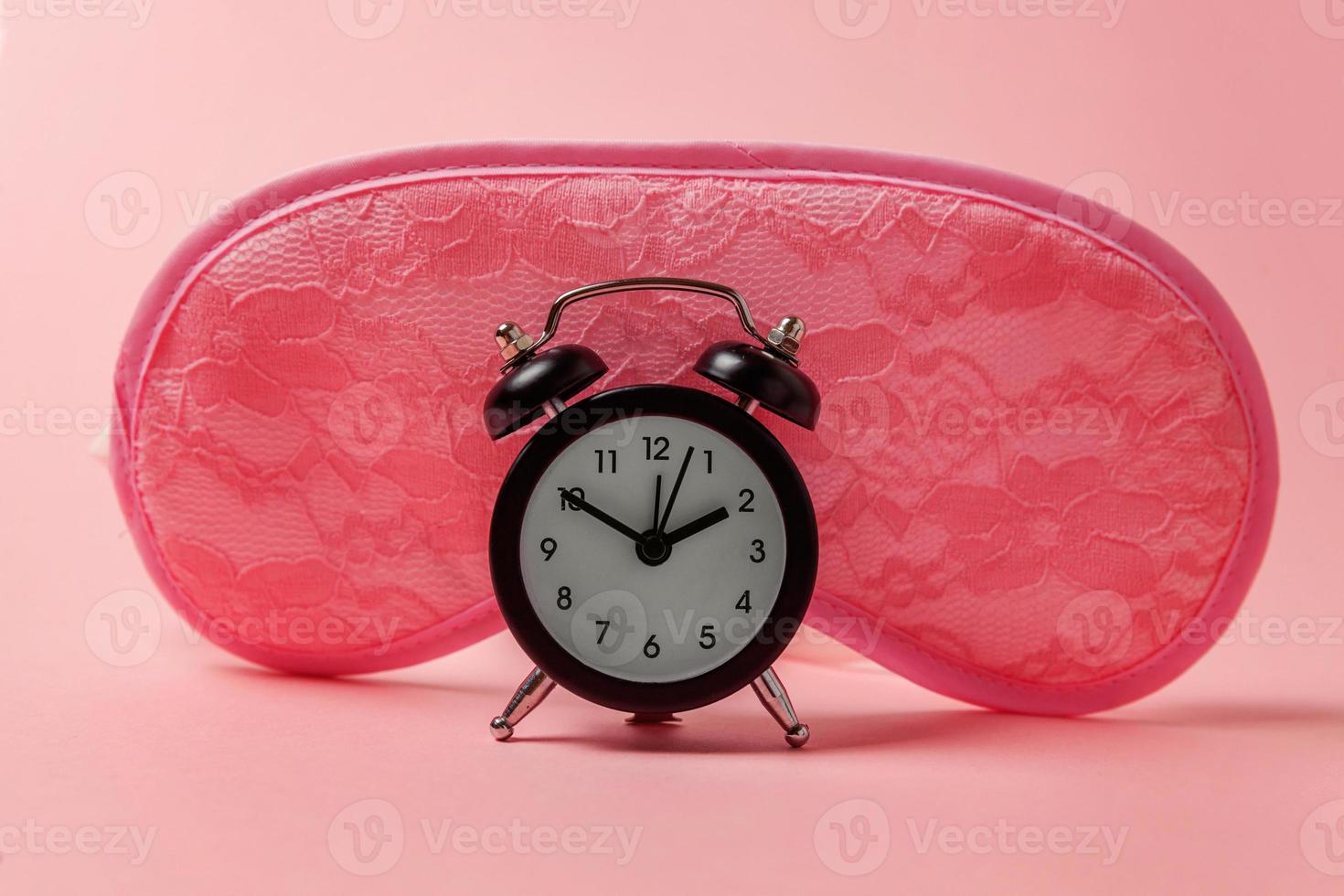 Sleeping eye mask, alarm clock isolated on pink pastel colourful trendy background. Do not disturb me, let me sleep. Rest, good night, siesta, insomnia, relaxation, tired, travel concept. photo