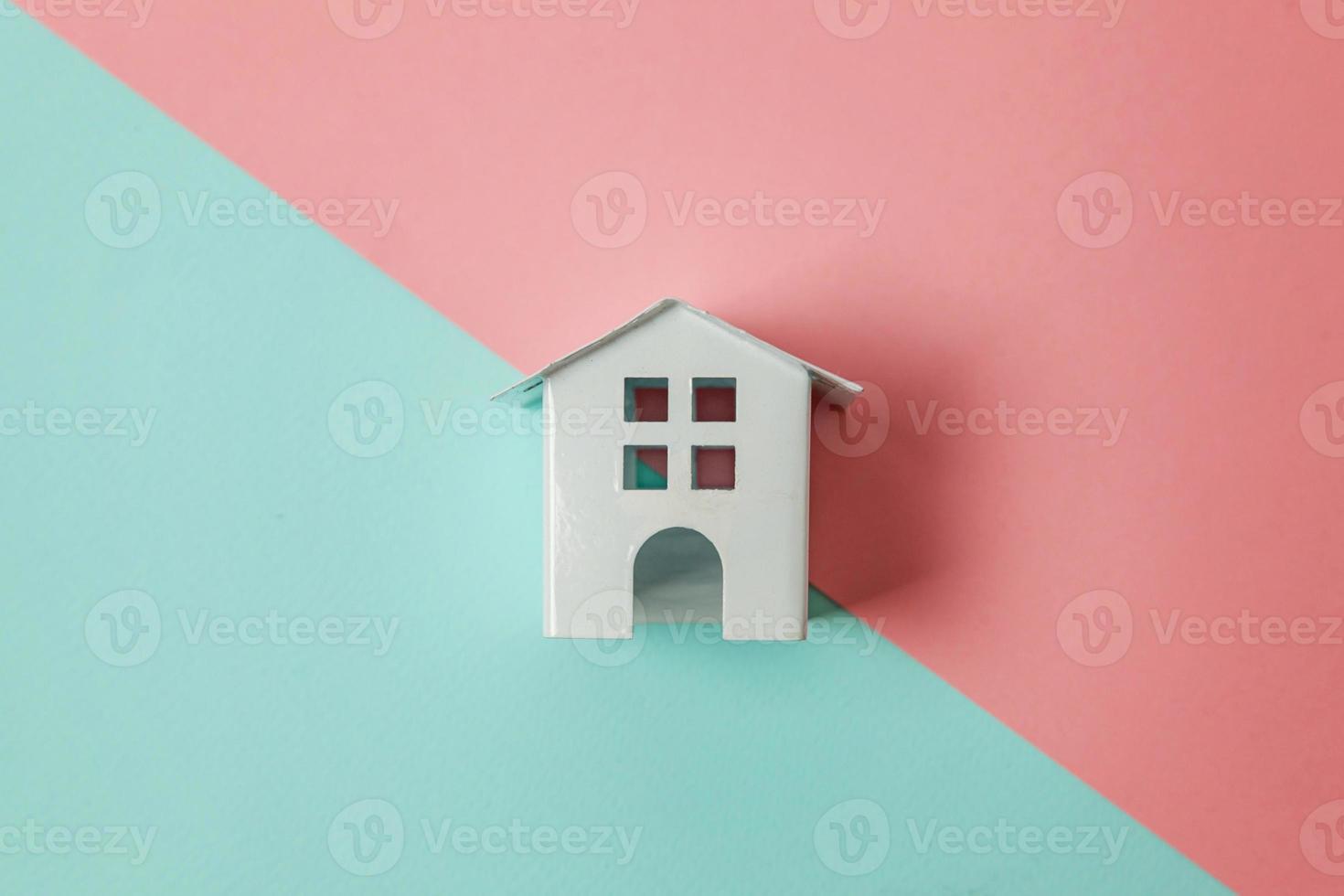 Simply design with miniature white toy house isolated on blue pink pastel colorful trendy geometric background. Mortgage property insurance dream home concept. Flat lay top view copy space. photo