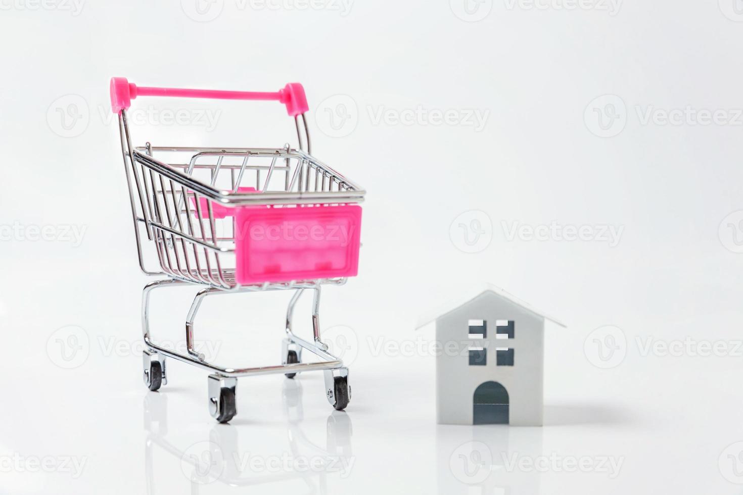 Simply design with miniature white toy house, supermarket grocery push cart for shopping isolated on white background. Mortgage property insurance dream home concept. Copy space. photo