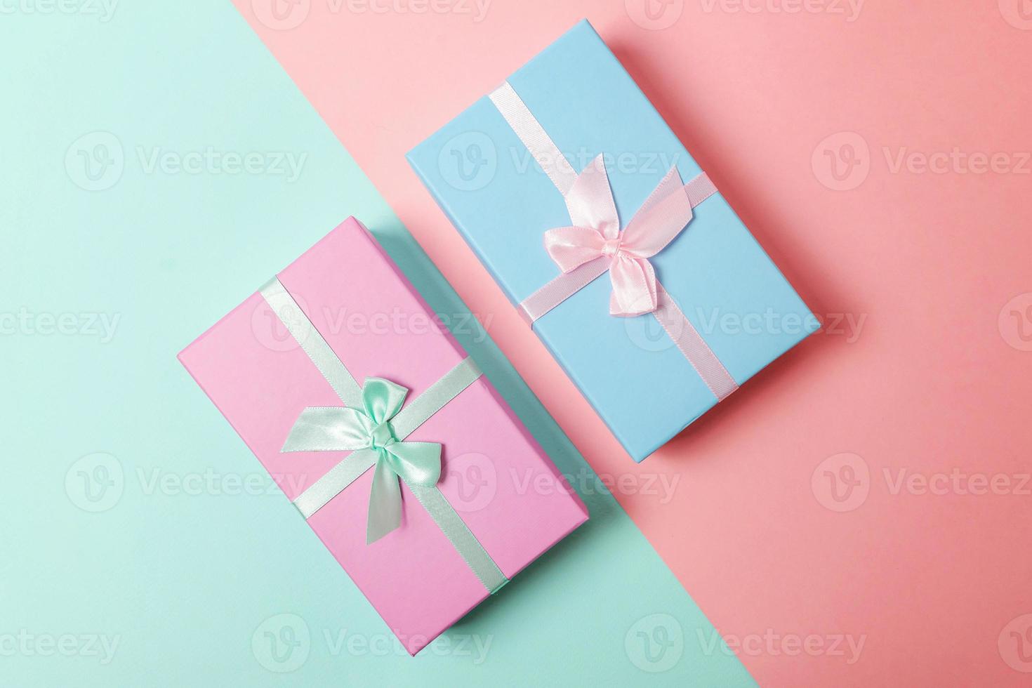 Small gift box wrapped pink and blue paper isolated on blue and pink pastel colorful trendy geometric background. Christmas New Year birthday valentine celebration present romantic concept. photo