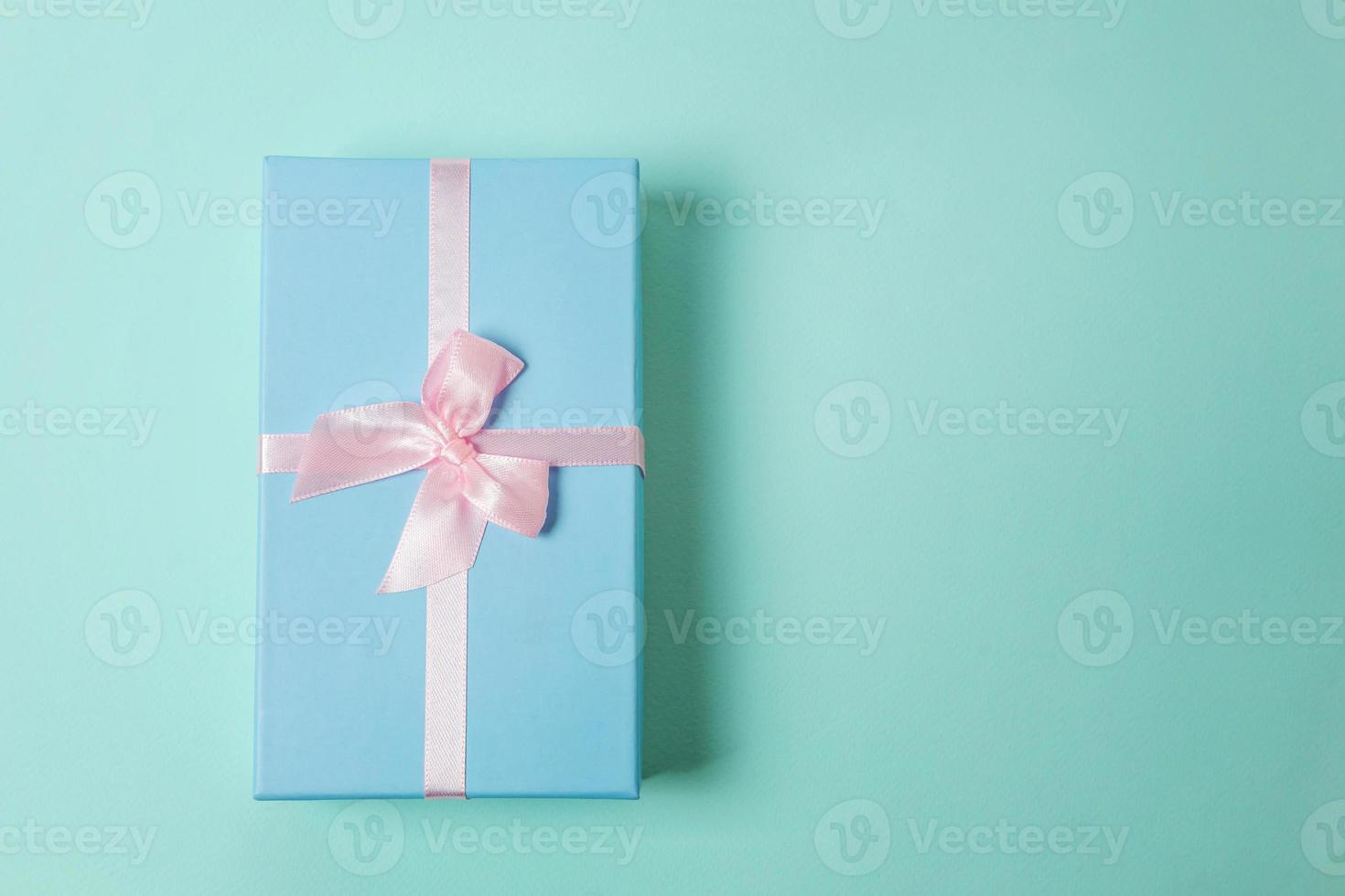 Small gift box wrapped blue paper isolated on pink pastel colorful trendy geometric background. Christmas New Year birthday valentine celebration present romantic concept. photo