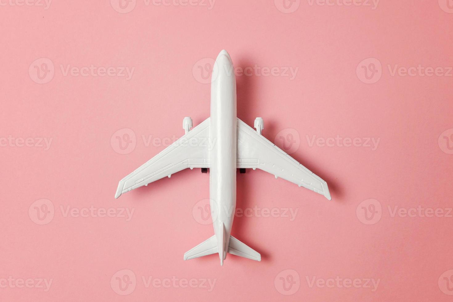 Simply flat lay design miniature toy model plane on pink pastel colorful paper trendy background. Travel by plane vacation summer weekend sea adventure trip journey ticket tour concept. photo