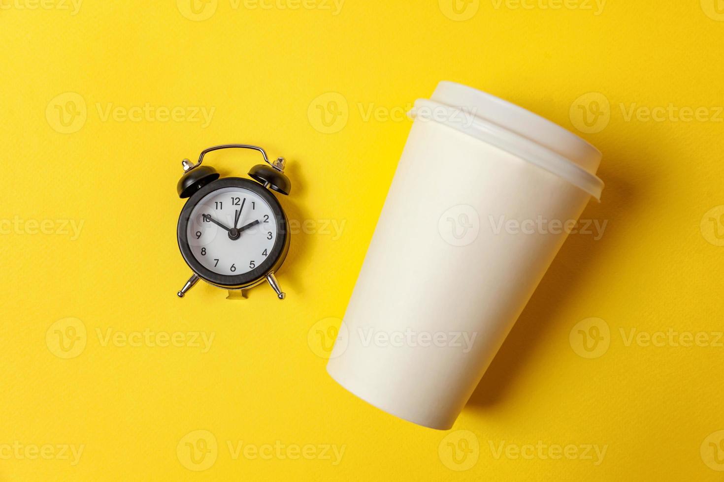 Simply flat lay design paper coffee cup and alarm clock on yellow colorful trendy background. Takeaway drink and breakfast beverage. Good morning wake up awake concept. Top view copy space. photo