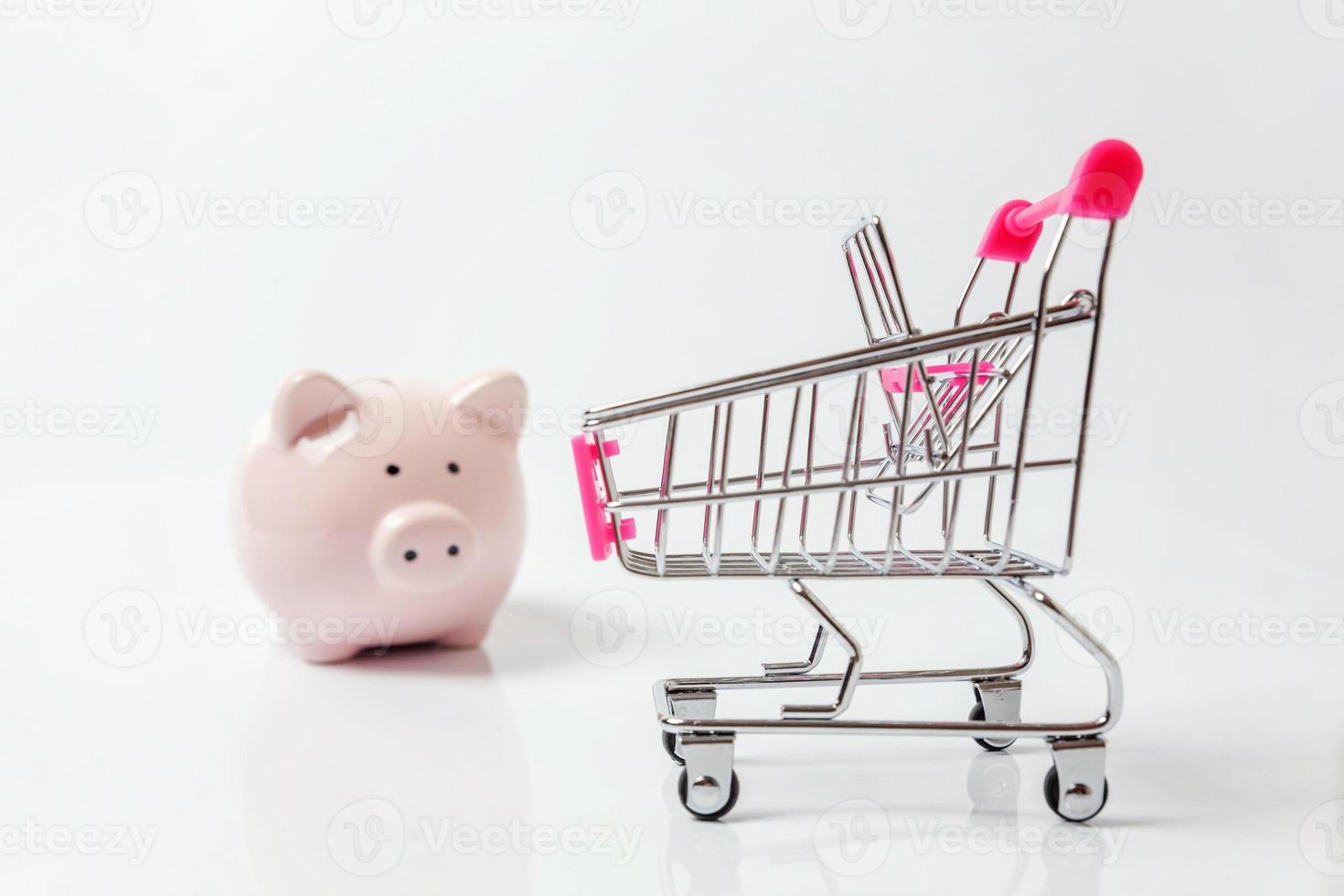 Small supermarket grocery push cart for shopping with piggy bank isolated on white background. Sale buy mall market shop consumer saving and budget concept. Copy space. photo