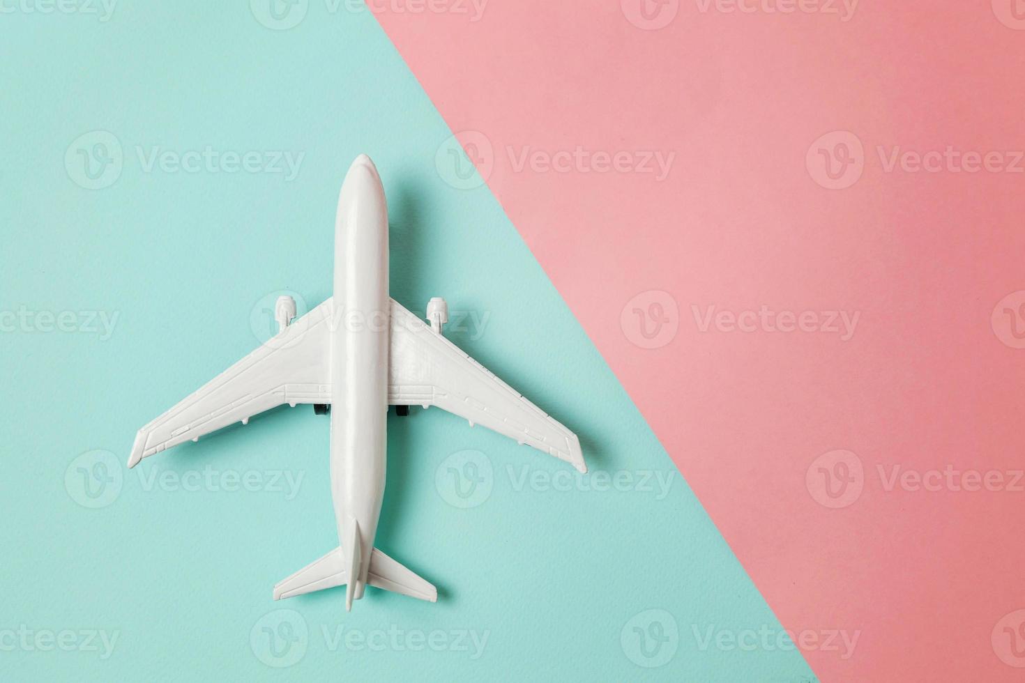 Simply flat lay design miniature toy model plane on blue and pink pastel colorful paper trendy geometric background. Travel by plane vacation summer weekend sea adventure trip concept. photo