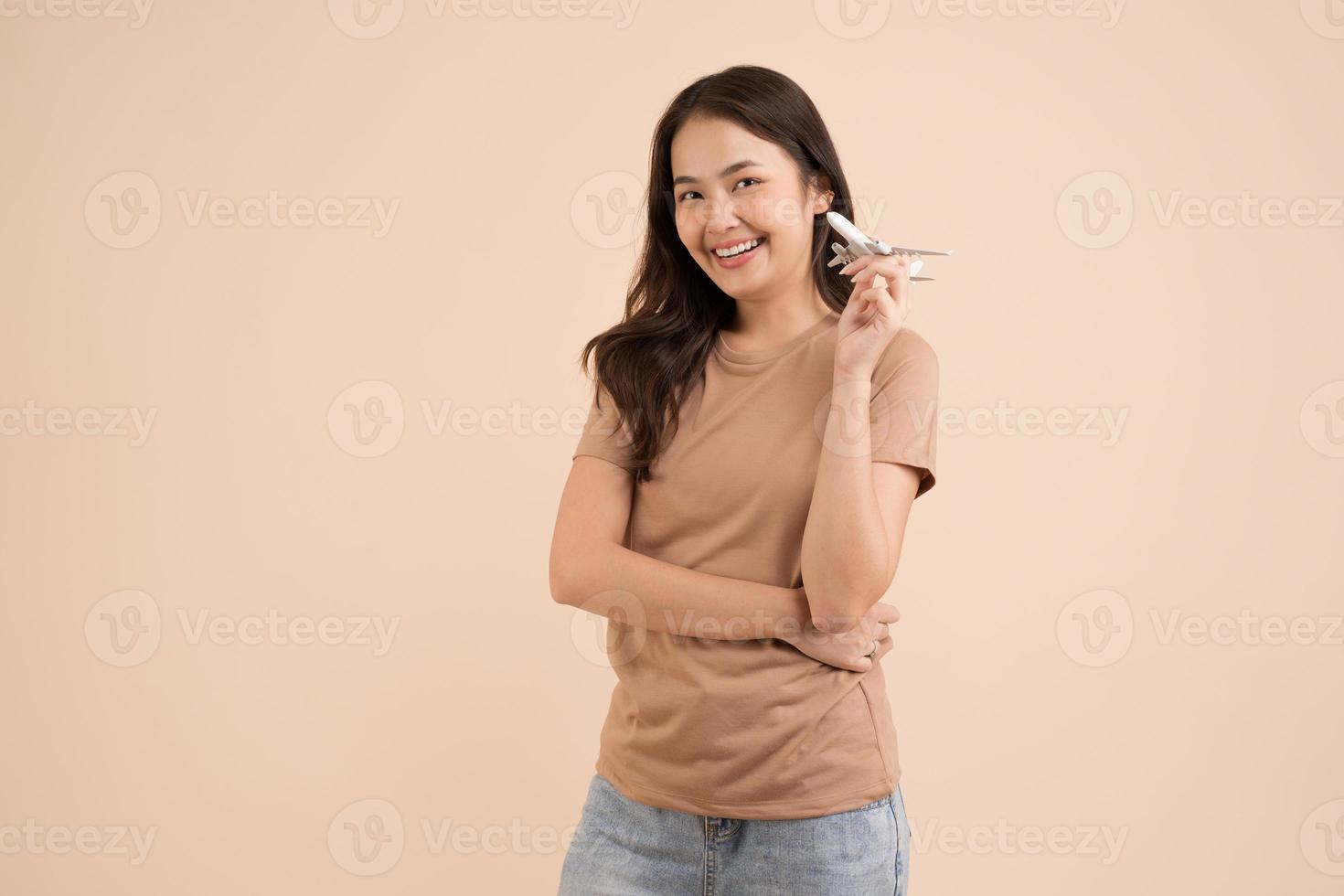 mujer joven feliz de pie y sosteniendo un avión de juguete blanco soñador en el estudio foto