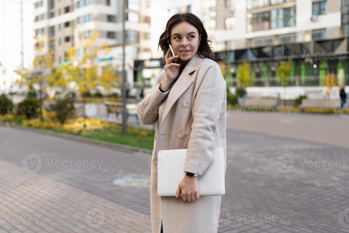 successful young business woman with a laptop in her hands speaks on a mobile phone against the backdrop of the city, strong and independent woman concept photo