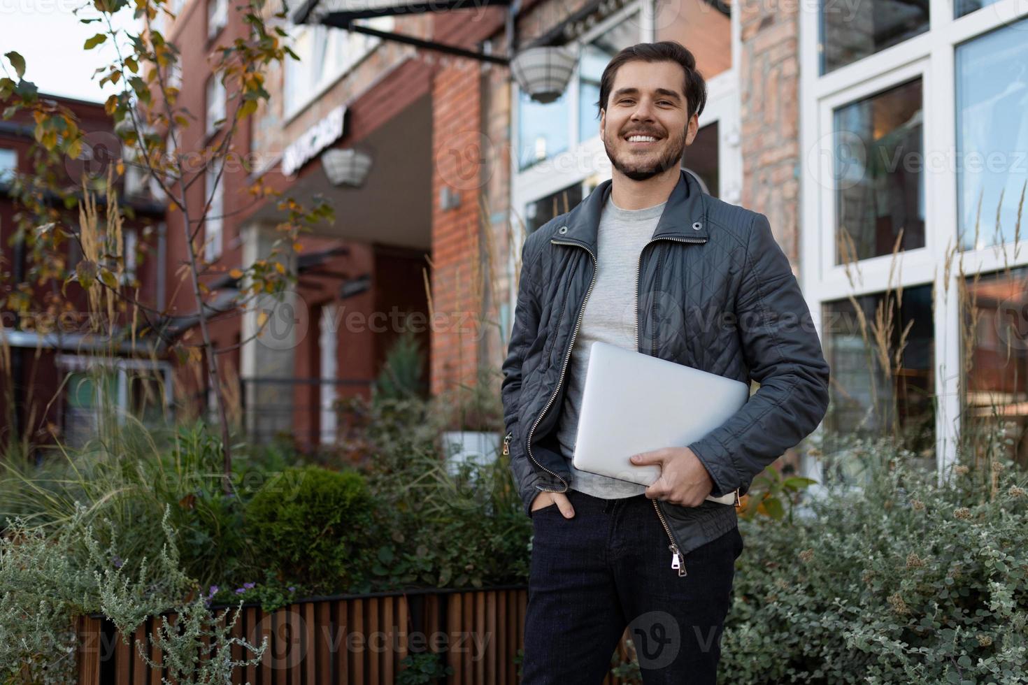 a satisfied male IT specialist with a laptop in his hands Ah stands smiling against the background of the entrance to the office photo