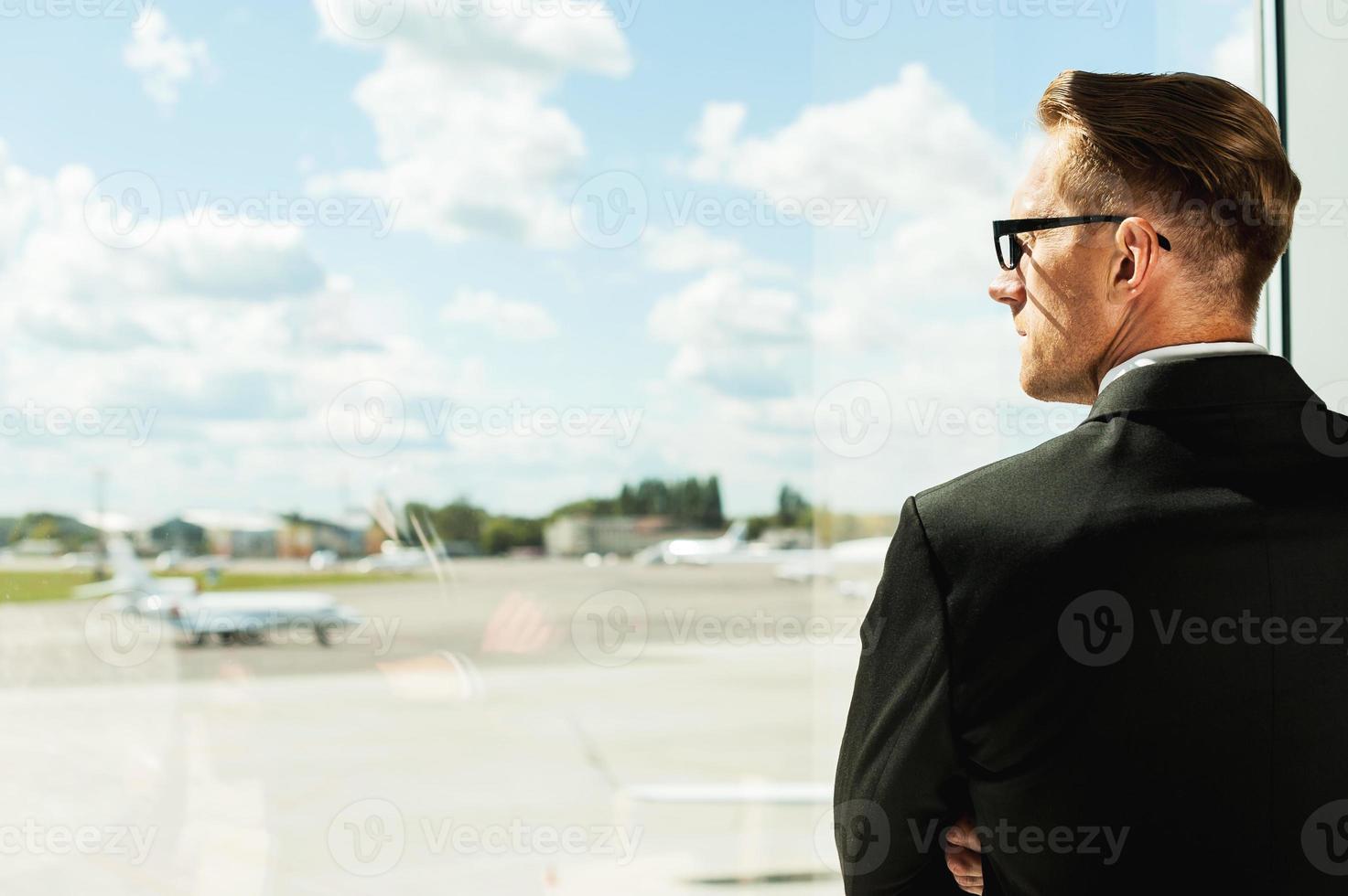 Waiting for his flight. Rear view of thoughtful businessman in formalwear looking through a window in airport photo
