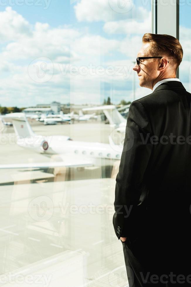 Waiting for flight. Rear view of thoughtful businessman in formalwear looking through a window in airport photo