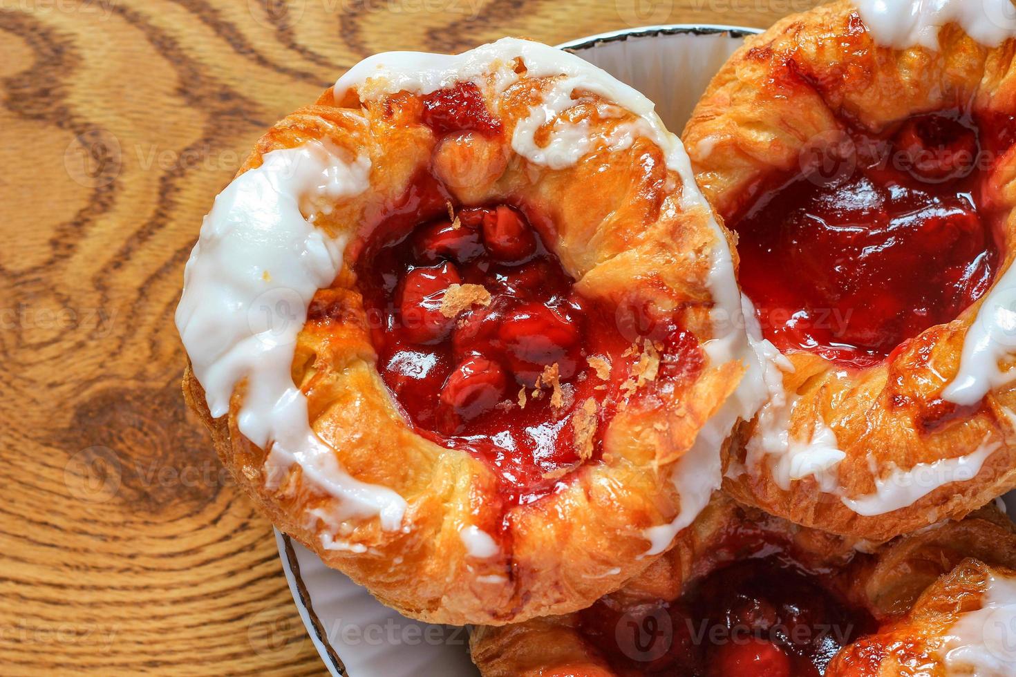 Cherry filled Danish or Danish bread served in a white plate on a brown wooden table. photo