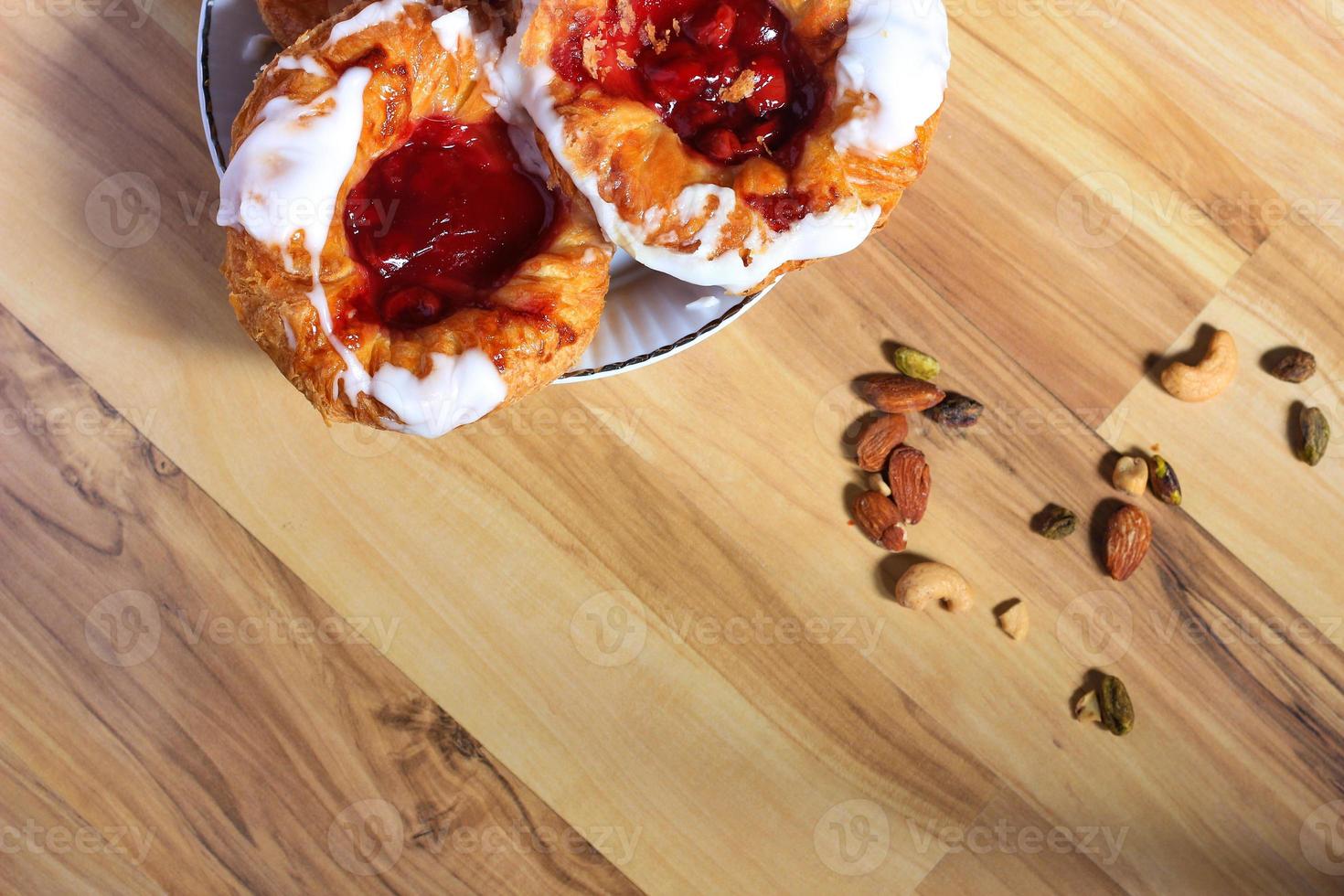 pan danés o danés relleno de cereza servido en un plato blanco sobre una mesa de madera marrón. foto