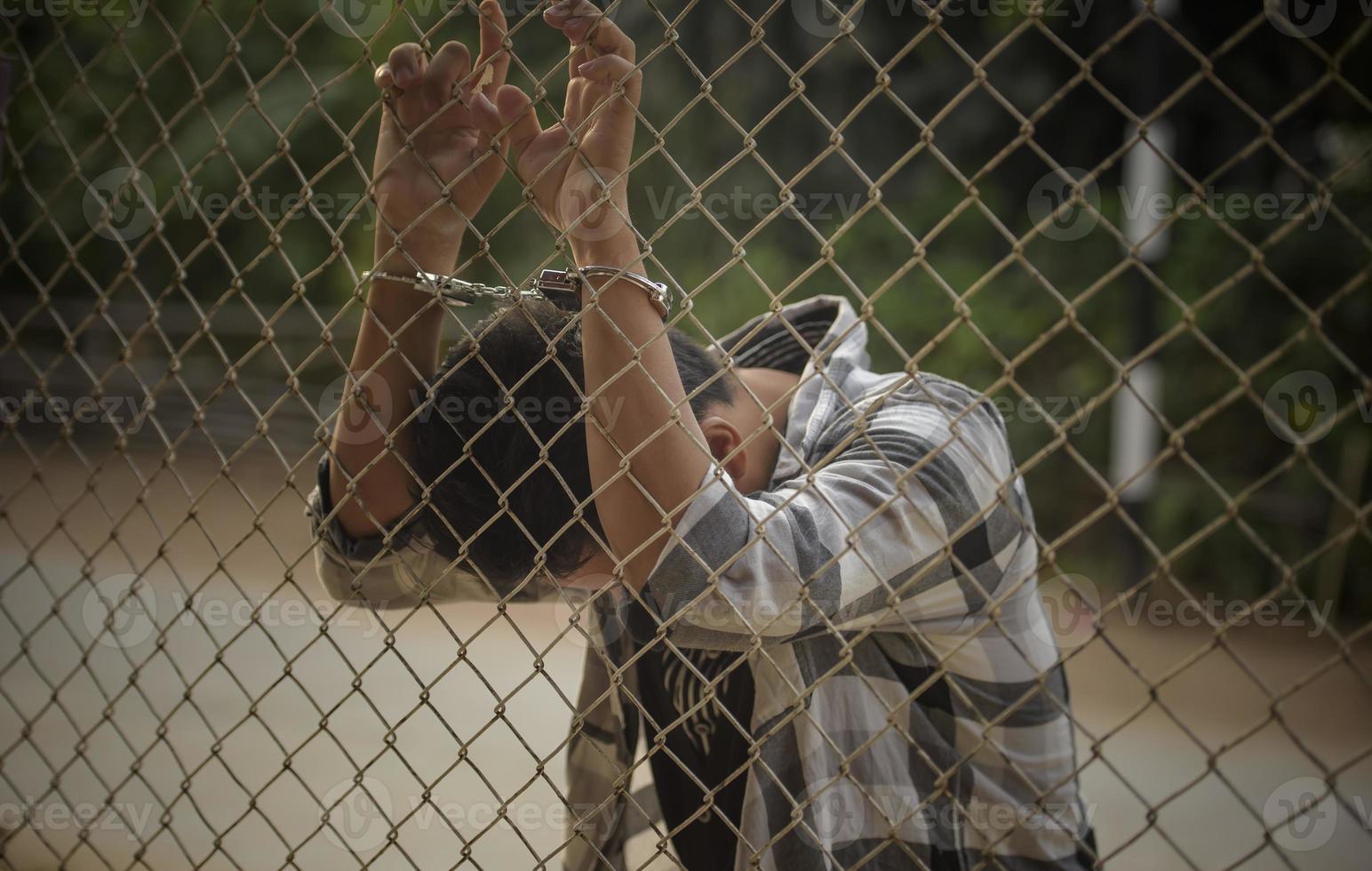 close-up photo of hands in prison steel mesh handle Handles the steel mesh cage, lacks independence.