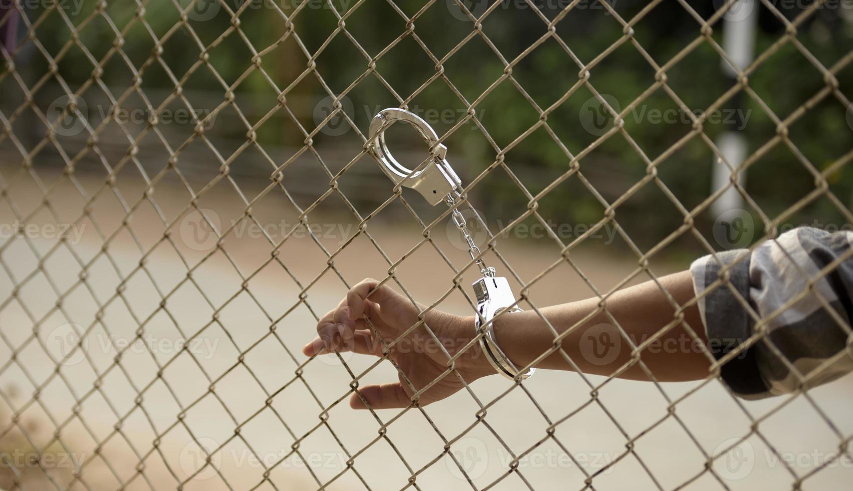 close-up photo of hands in prison steel mesh handle Handles the steel mesh cage, lacks independence.