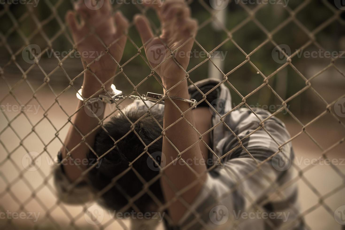 close-up photo of hands in prison steel mesh handle Handles the steel mesh cage, lacks independence.