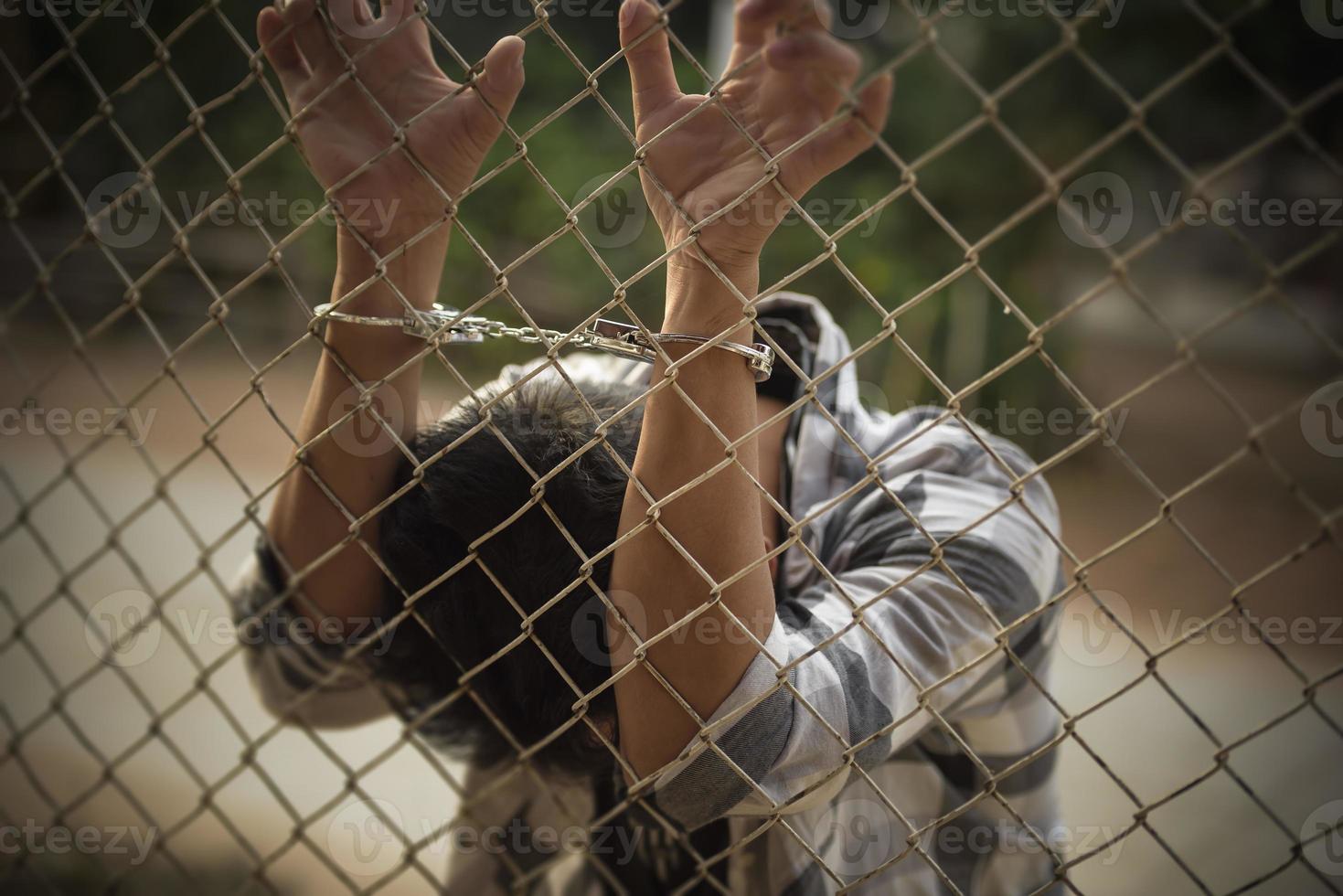 close-up photo of hands in prison steel mesh handle Handles the steel mesh cage, lacks independence.