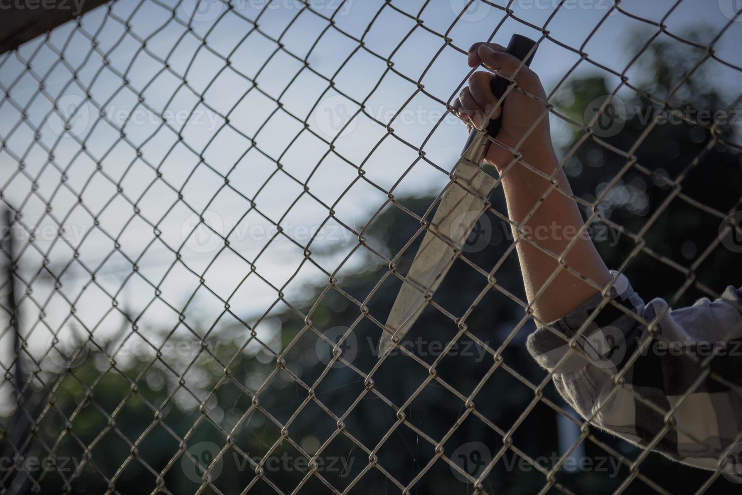 close-up photo of hands in prison steel mesh handle Handles the steel mesh cage, lacks independence.