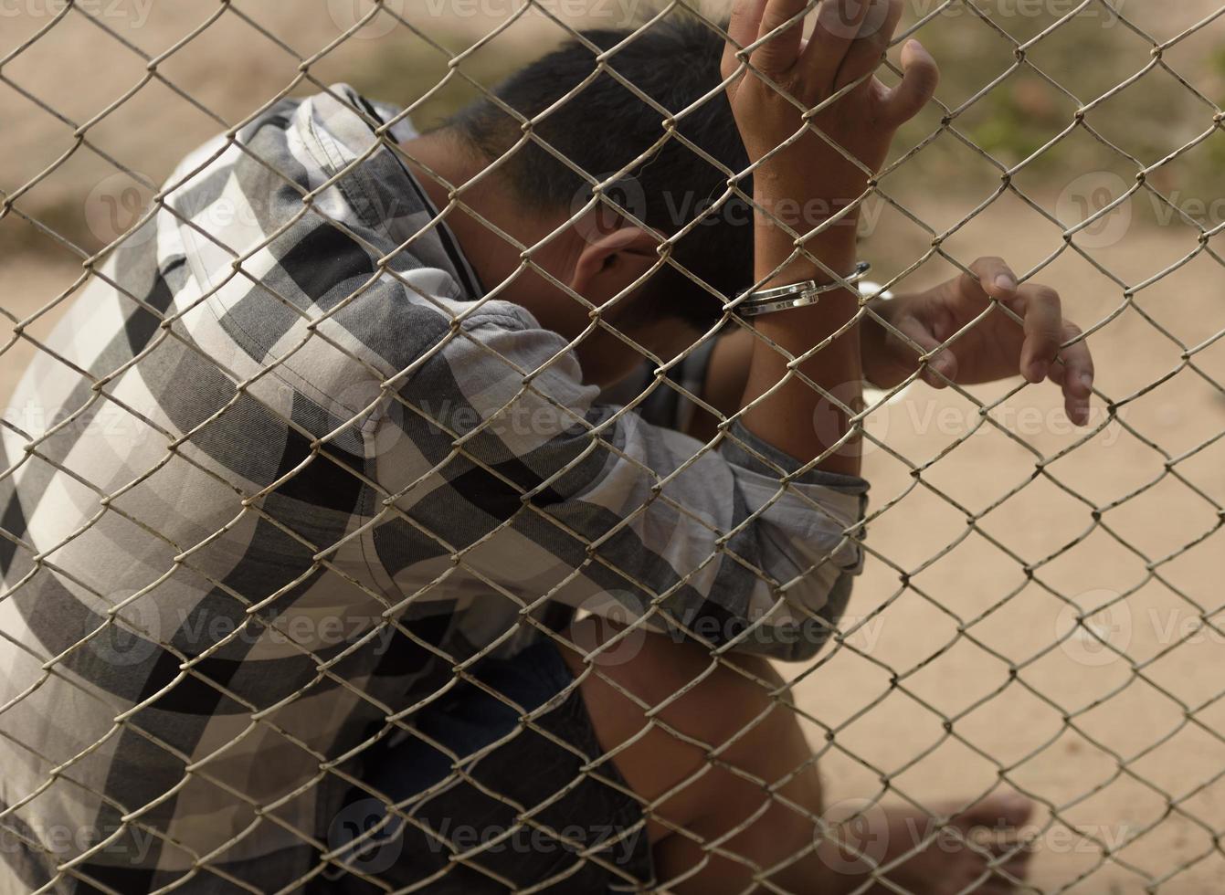 close-up photo of hands in prison steel mesh handle Handles the steel mesh cage, lacks independence.