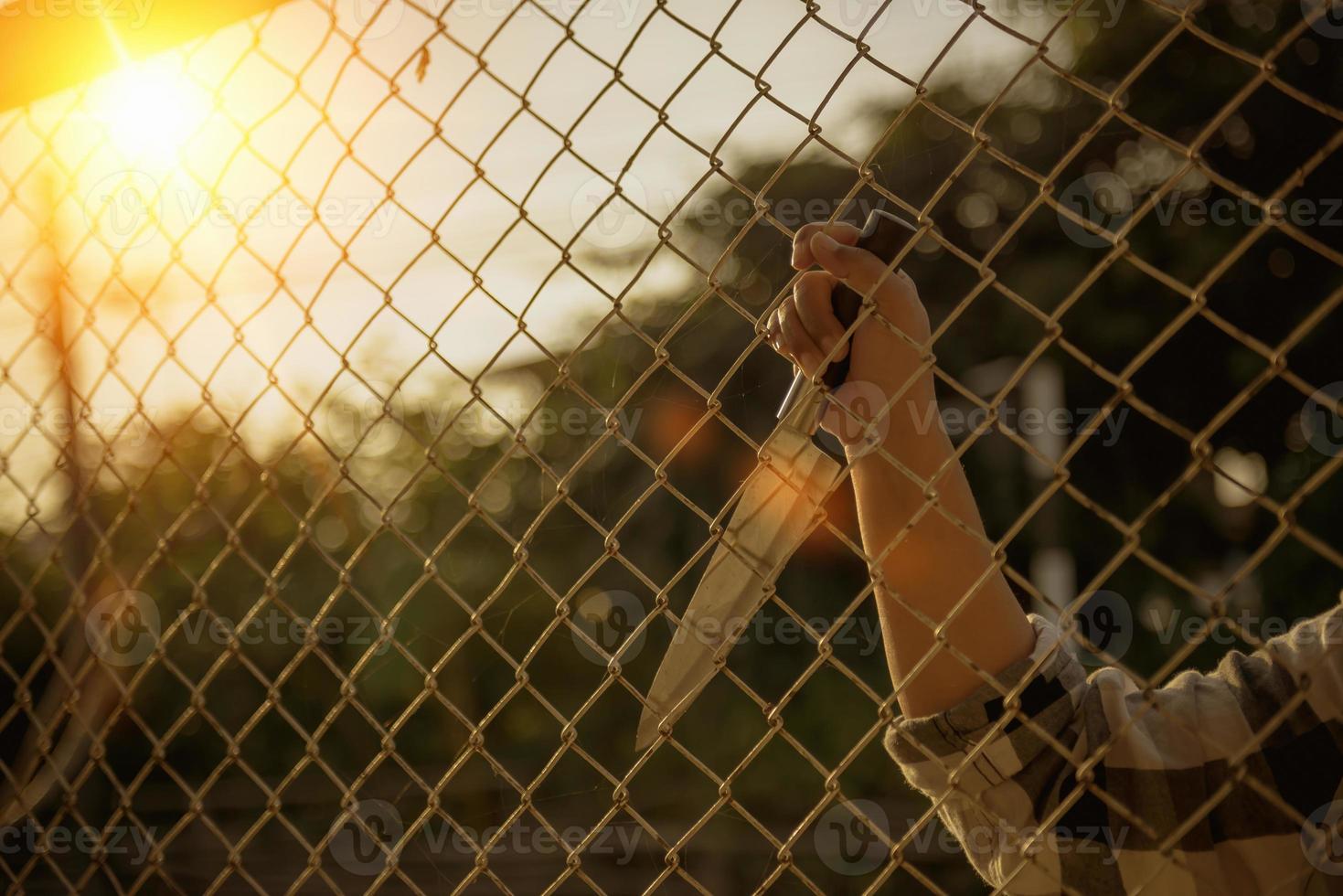 close-up photo of hands in prison steel mesh handle Handles the steel mesh cage, lacks independence.