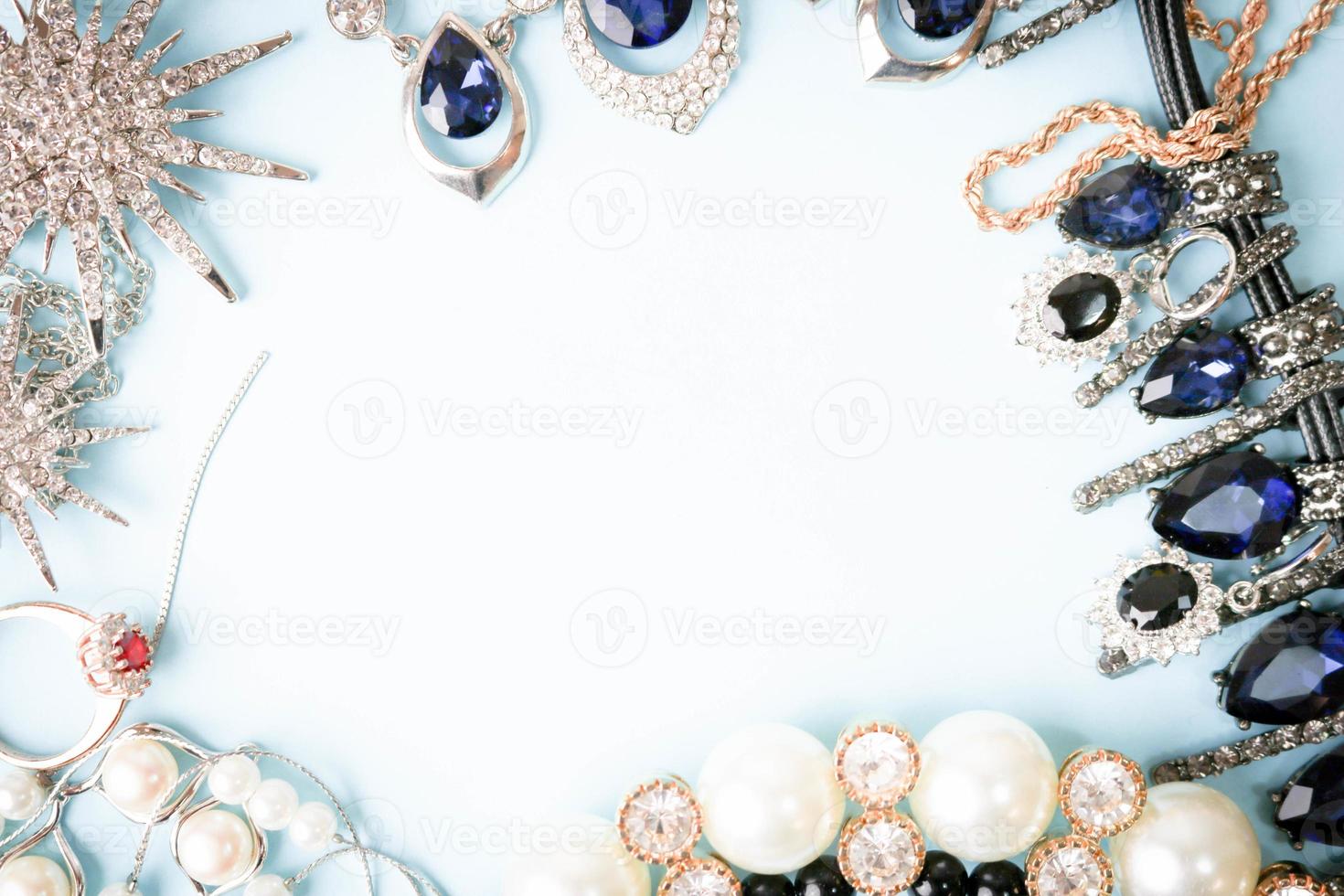 Beautiful precious shiny jewelery trendy glamorous jewelry set, necklace, earrings, rings, chains, brooches with pearls and diamonds on a blue background. Flat lay, top view, copy place photo