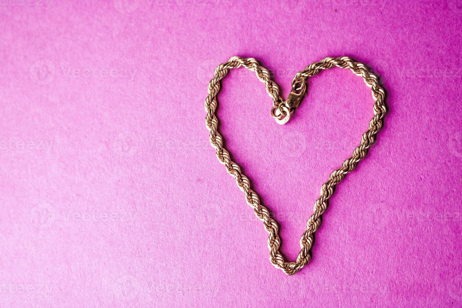 Texture of a beautiful golden festive chain unique weaving in the shape of a heart on a pink purple background and copy space. Concept love, marriage proposal, marriage, St. Valentine's Day photo