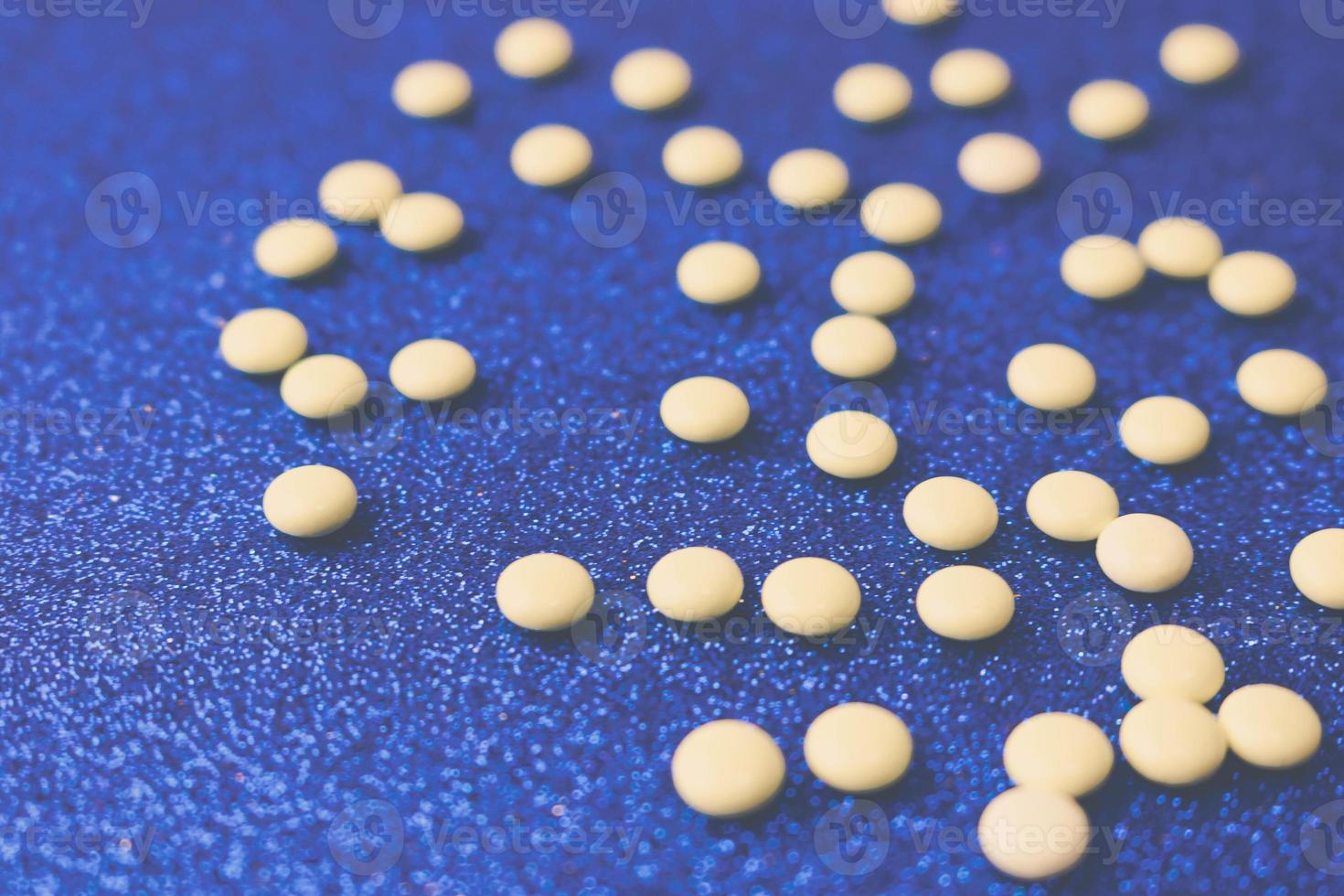 Small yellow orange beautiful medical pharmaceptic round pills, vitamins, drugs, antibiotics on a blue background, texture. Concept medicine, health care. Flat lay, top view photo