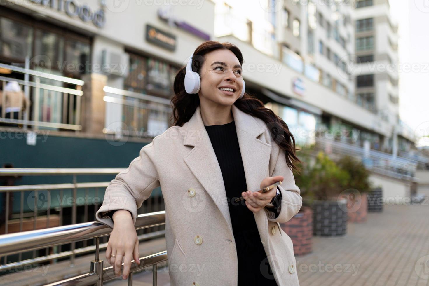 mujer joven y elegante escuchando música con auriculares con una gran sonrisa en la cara fuera de la oficina foto