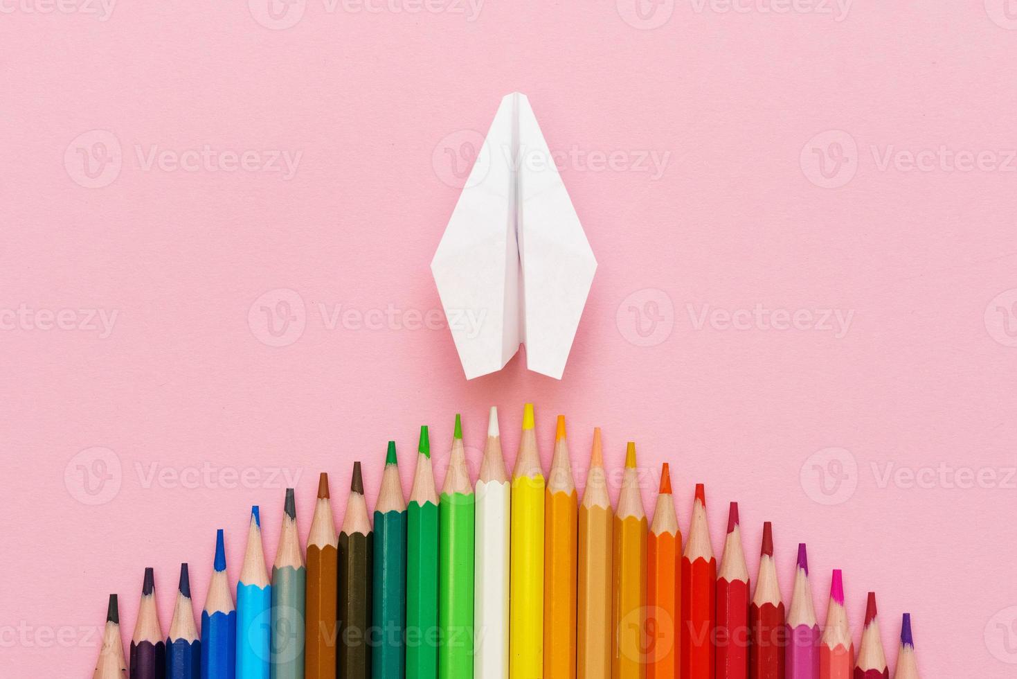 Paper plane, wood colored pencils, flat dip on pink background, top view. photo