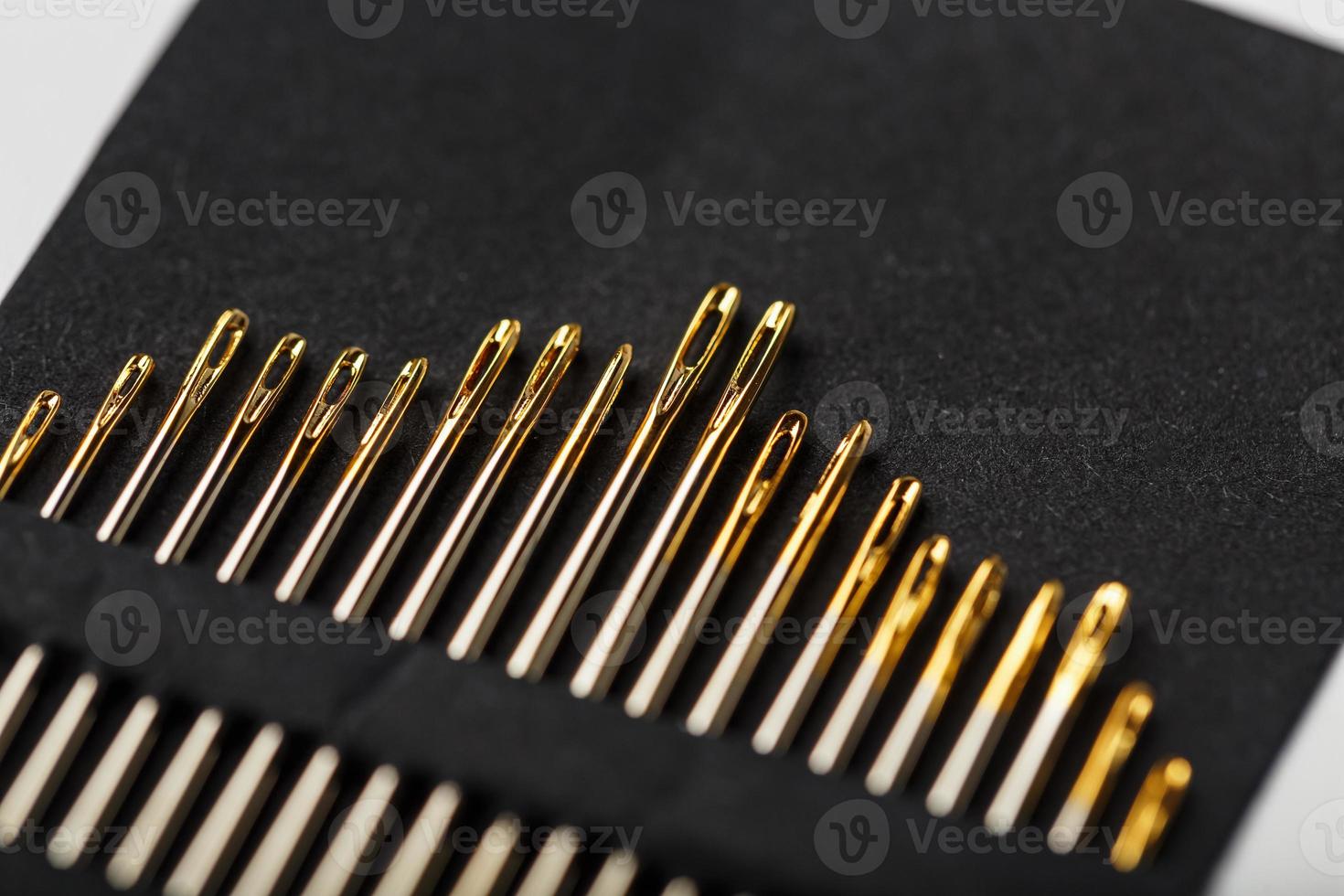 Gold sewing needles on a black background in a row. photo