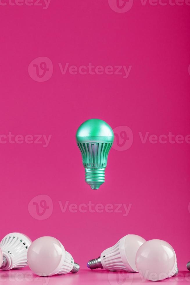 A special Light bulb hovers over simple, standard white light bulbs on a pink background. photo