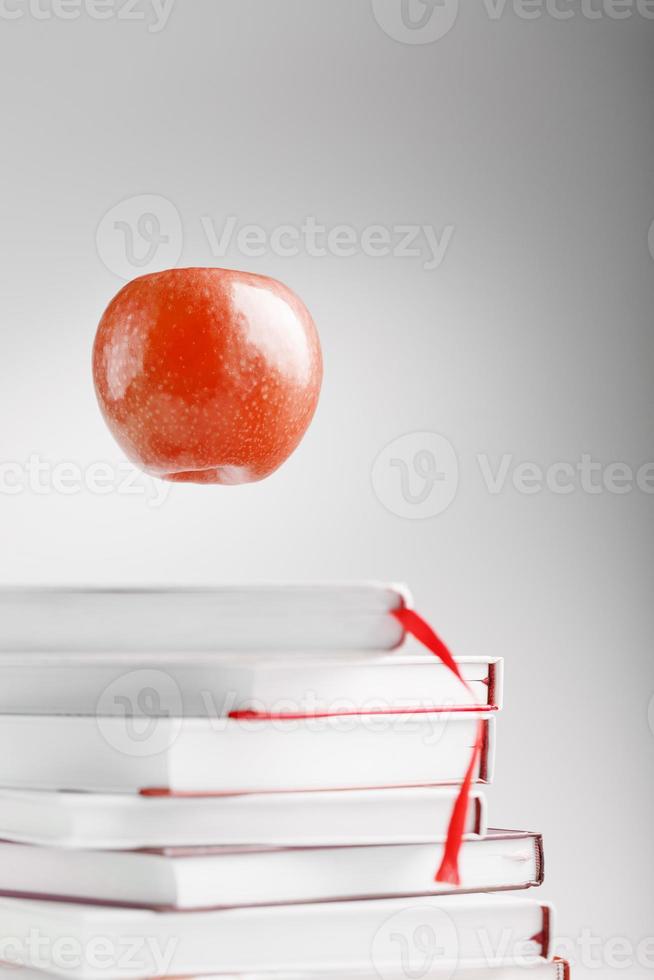 una manzana roja cuelga sobre los libros sobre un fondo blanco. foto