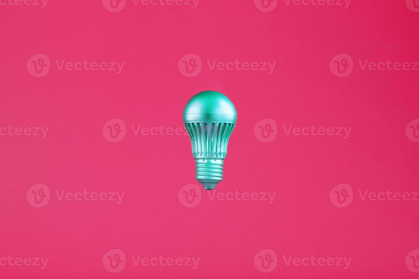 The light bulb hovers in the center of the frame in an isolated space on a pink background. photo