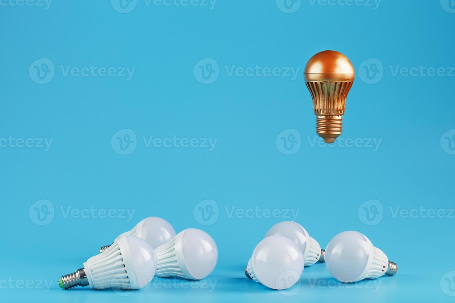 A prominent gold light bulb levitates above an environment of white led bulbs. photo