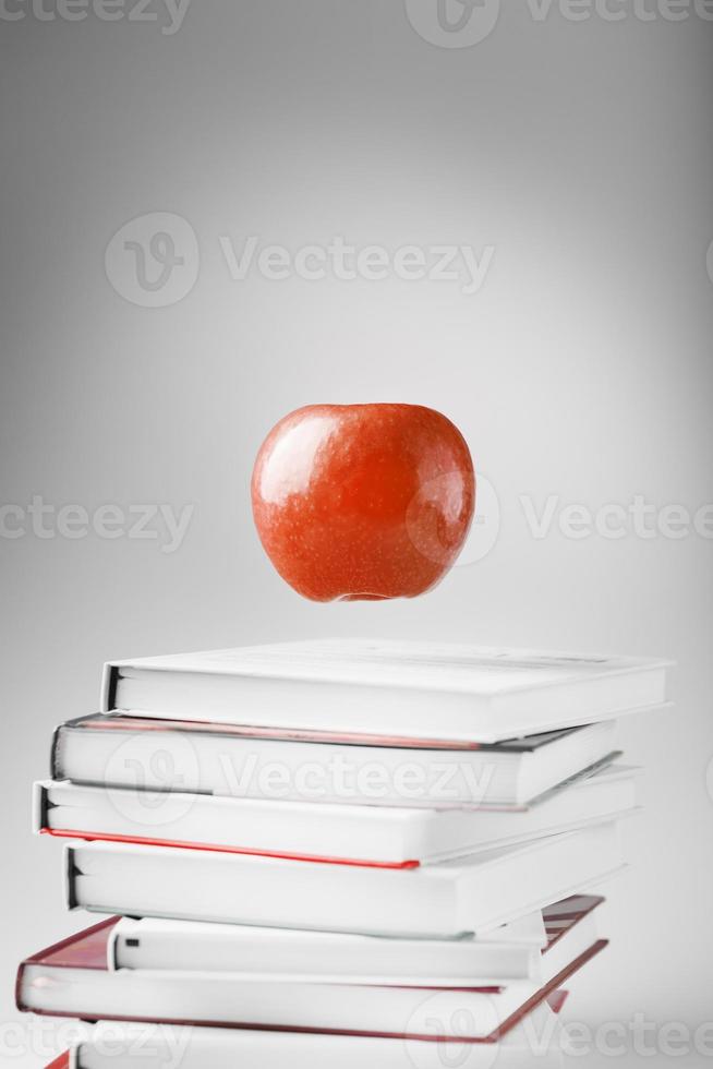 una manzana roja cuelga sobre los libros sobre un fondo blanco. foto