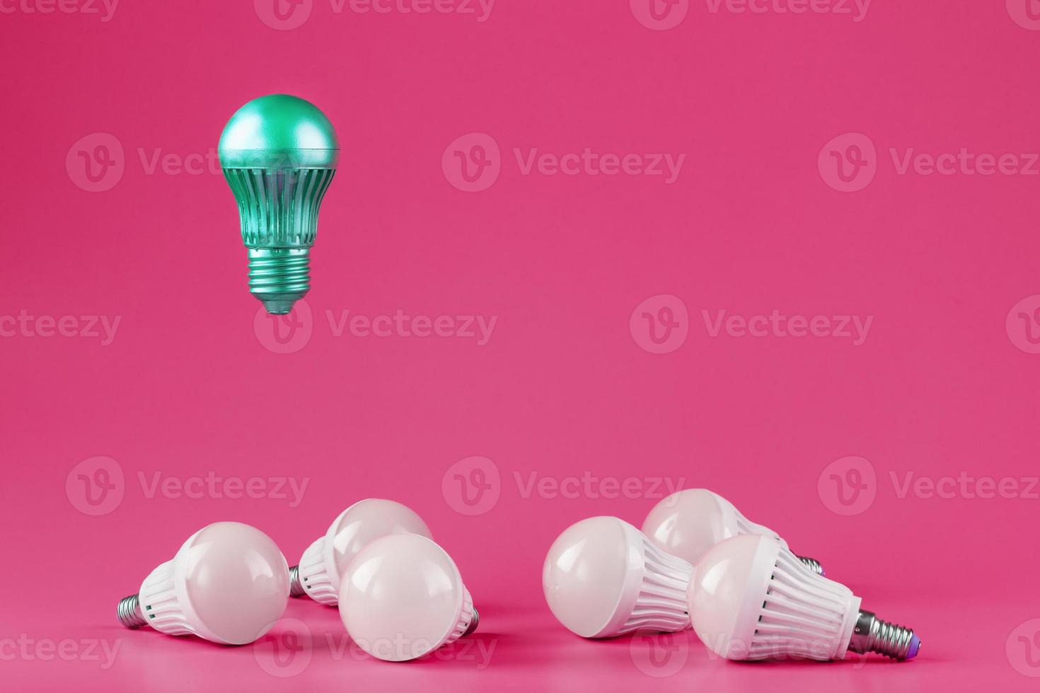 A special Light bulb hovers over simple, standard white light bulbs on a pink background. photo