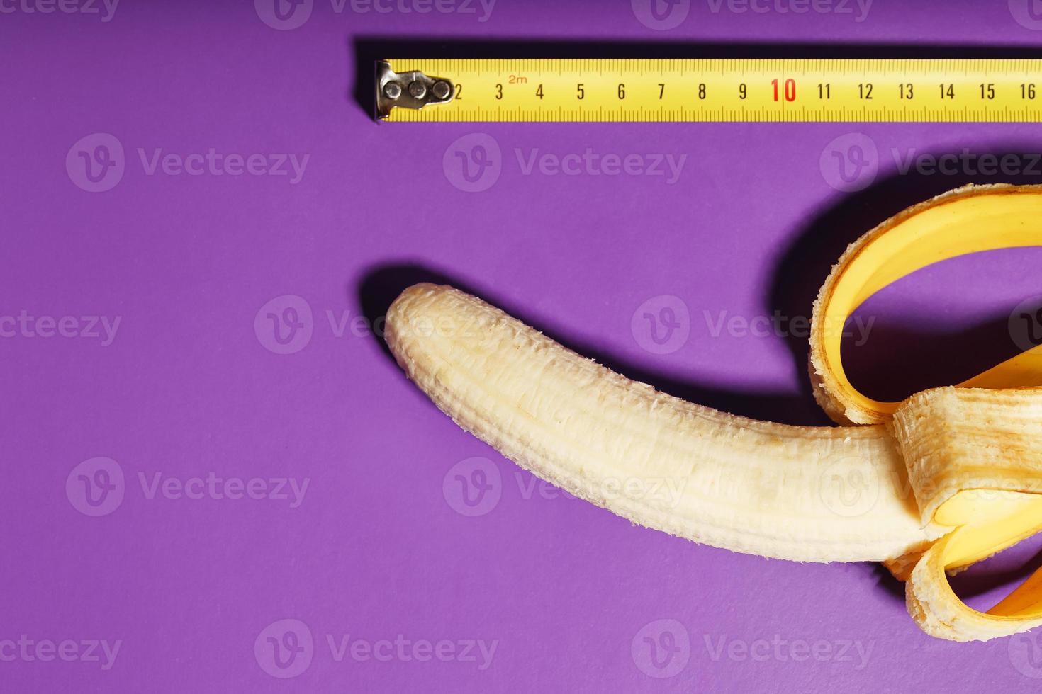 concepto de pene de plátano amarillo medido con cinta métrica sobre fondo rosa. comparación del tamaño de la dignidad de un hombre. foto