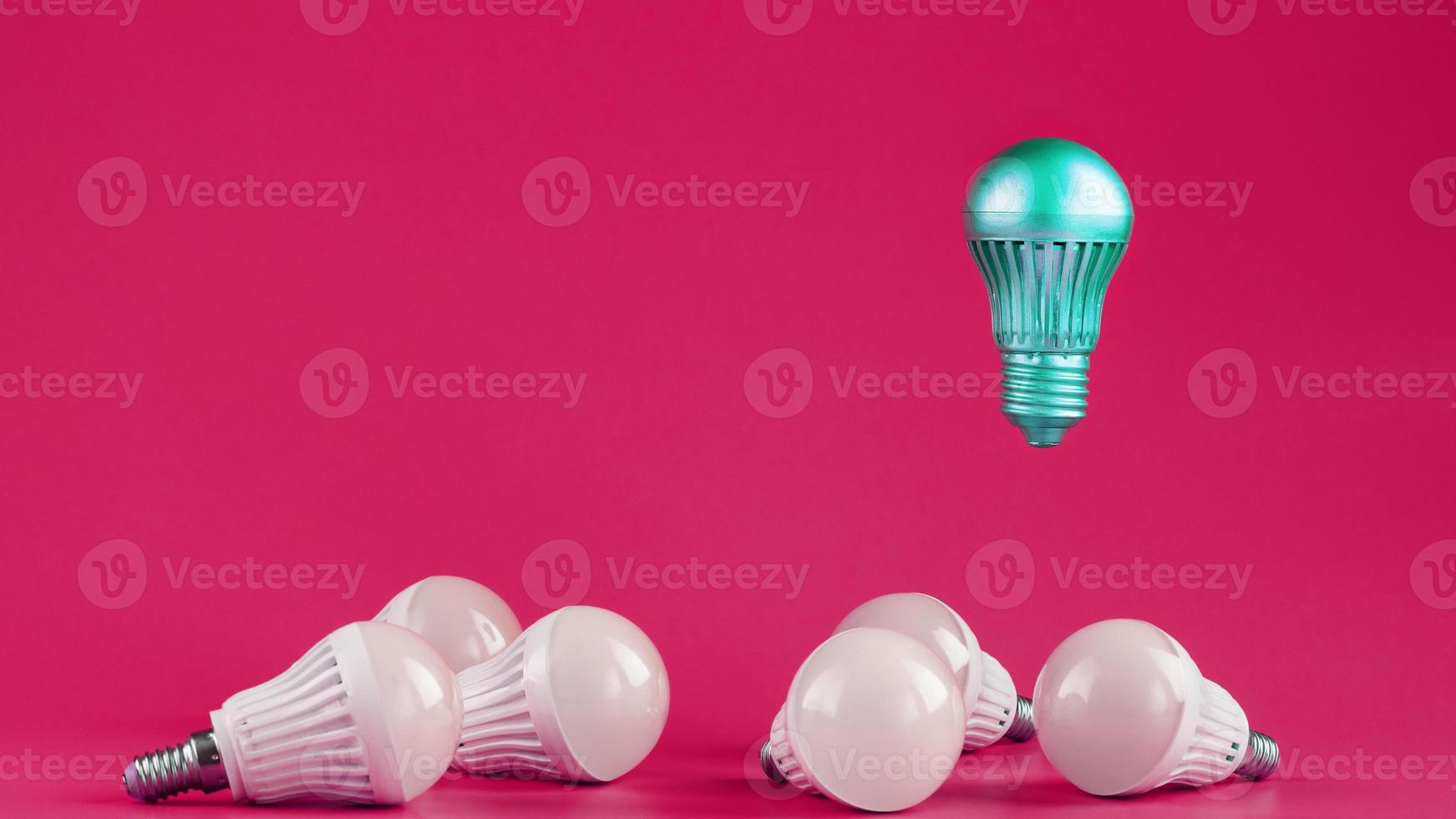 A special Light bulb hovers over simple, standard white light bulbs on a pink background. photo