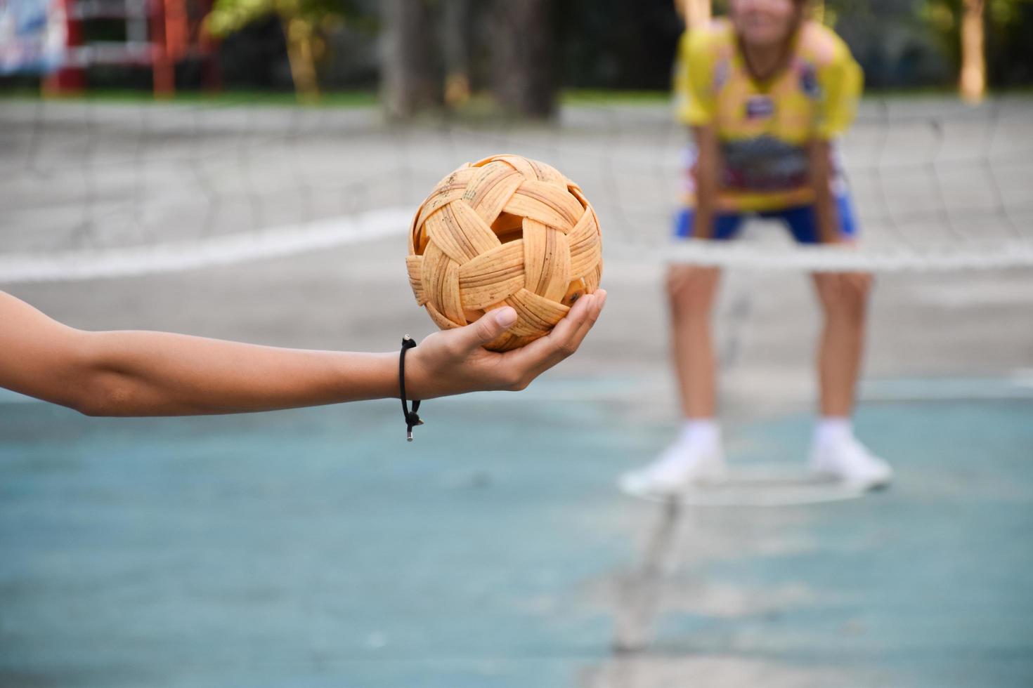 pelota de sepak takraw, deporte tradicional de los países del sudeste asiático, sosteniendo en la mano a una joven jugadora asiática de sepak takraw frente a la red antes de arrojársela a otro jugador para que patee la red. foto