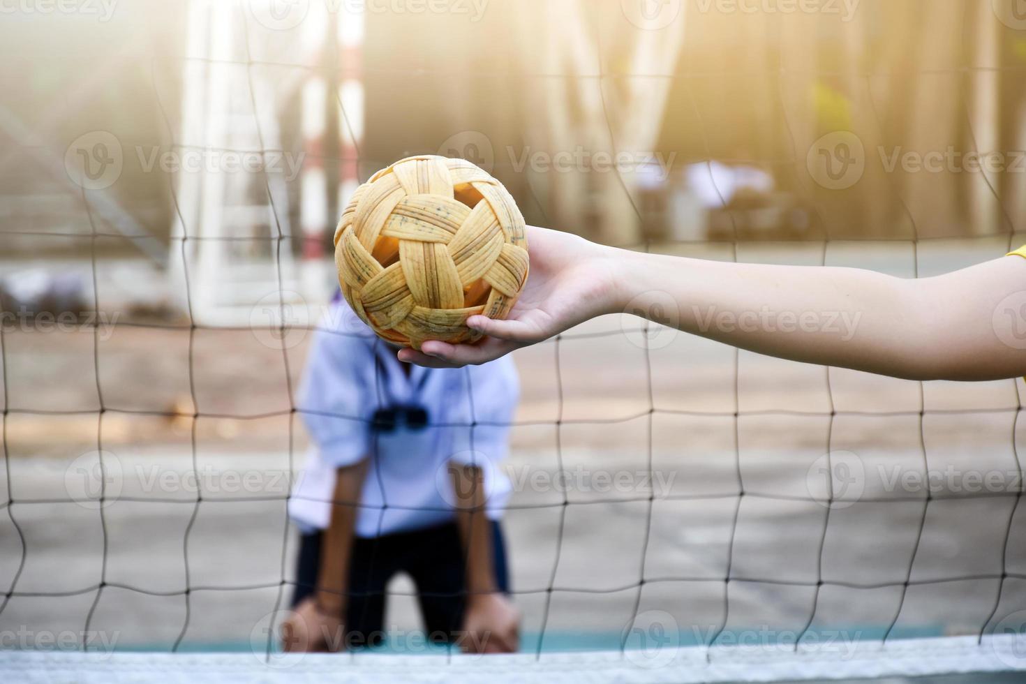 Sepak takraw ball, southeast asian countries traditional sport, holding in hand of young asian female sepak takraw player in front of the net before throwing it to another player to kick over the net. photo