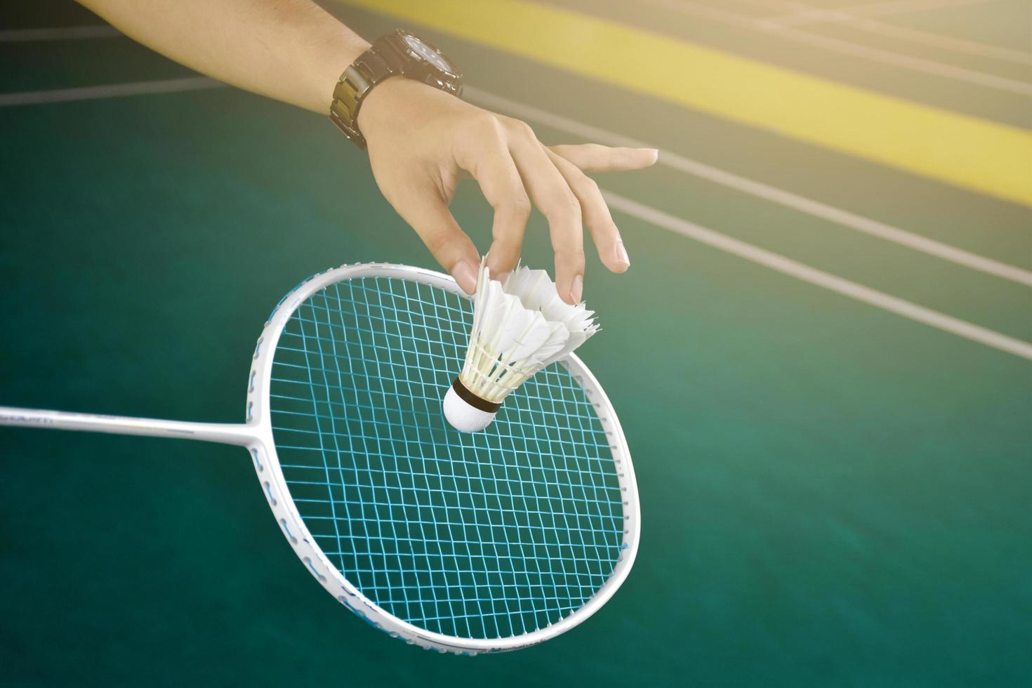 Badminton player holds racket and white cream shuttlecock in front of the net before serving it to another side of the court. photo