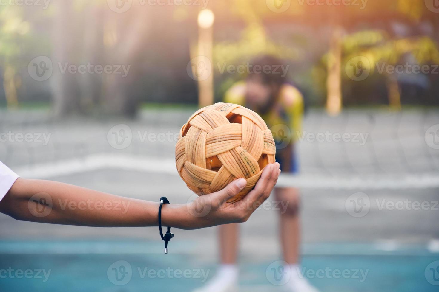 Sepak takraw ball, southeast asian countries traditional sport, holding in hand of young asian female sepak takraw player in front of the net before throwing it to another player to kick over the net. photo