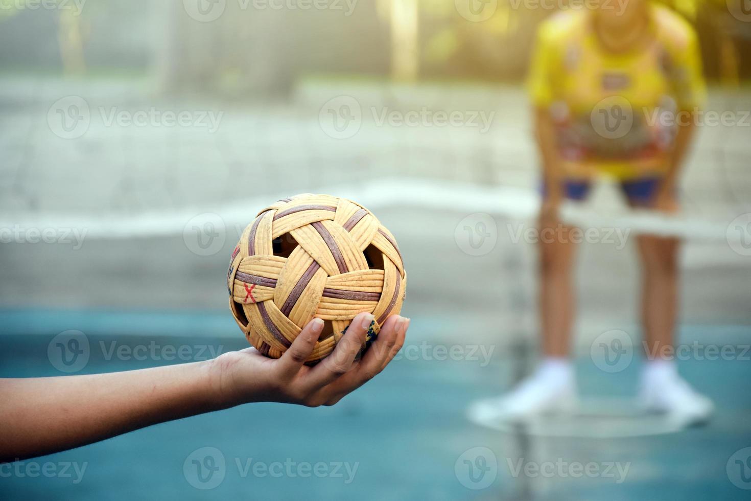 Sepak takraw ball, southeast asian countries traditional sport, holding in hand of young asian female sepak takraw player in front of the net before throwing it to another player to kick over the net. photo